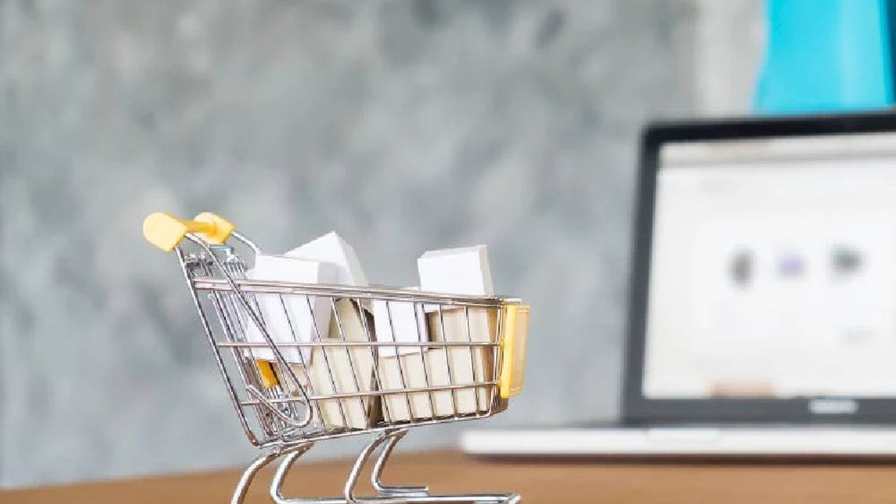 A mini shopping cart on a desk next to a laptop